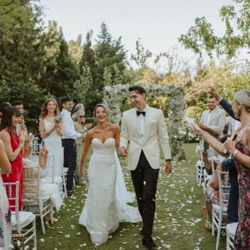 this is a photo of a happy young couple walking down the outdoor aisle at their wedding, with their family and friends cheering in Marbella.